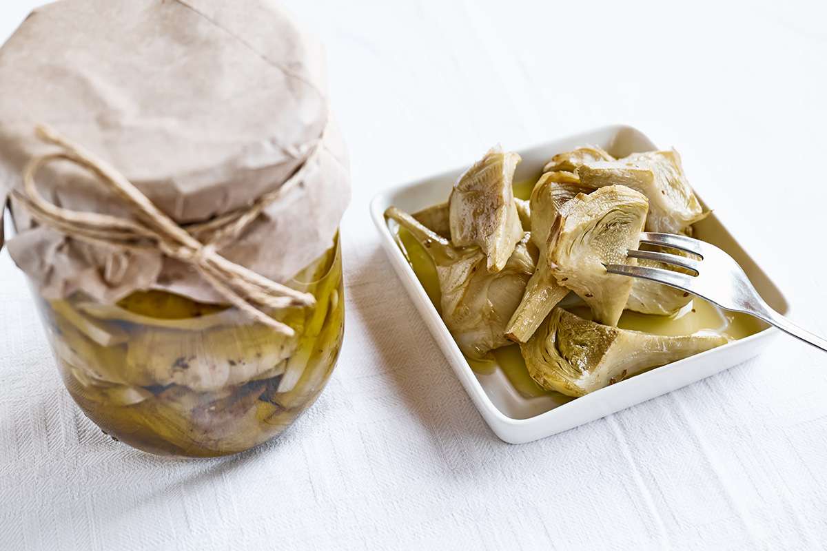 barattolo di carciofini sott olio e vaschetta bianca con carciofini in forchetta